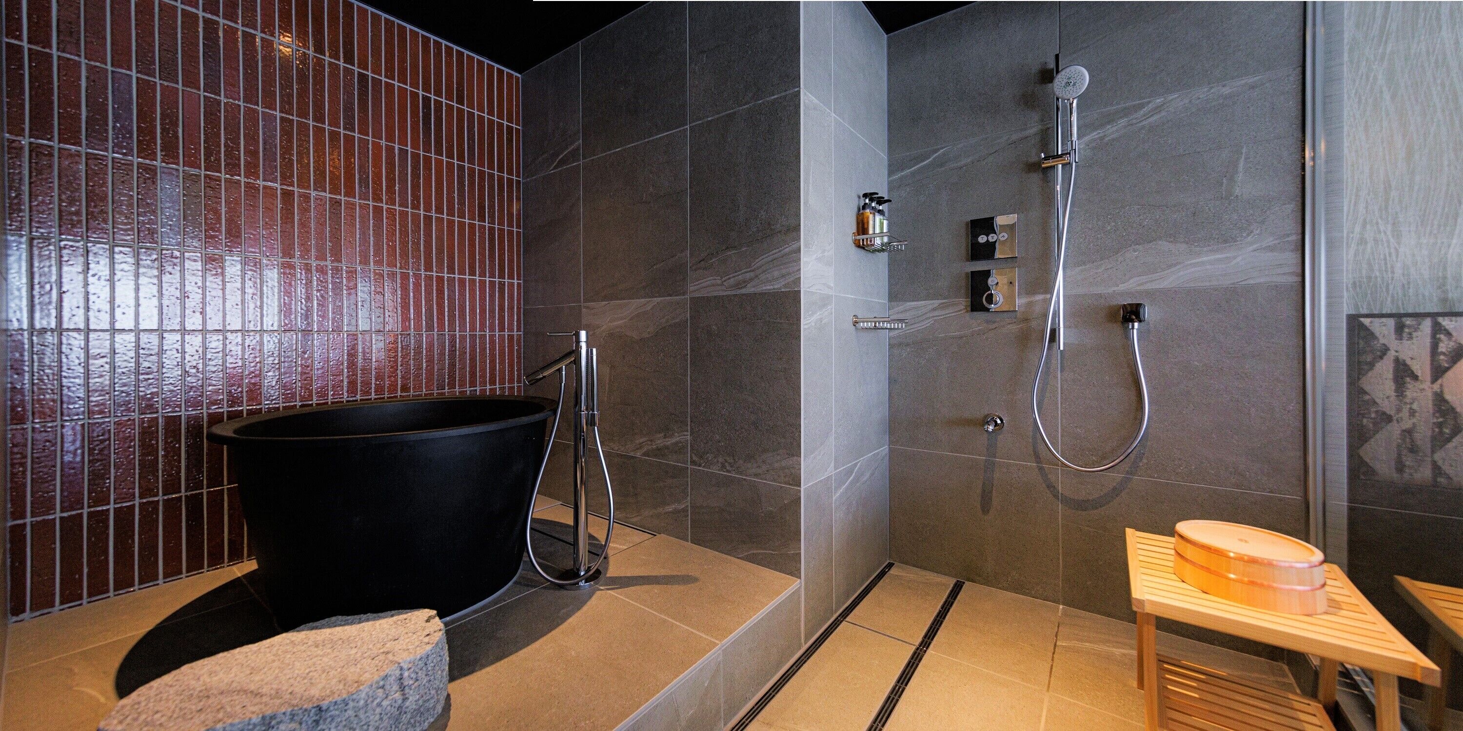 A modern bathroom with a large black bathtub, a shower area, and a wooden stool.