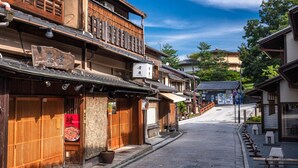 En traditionel japansk gade med træbygninger, et skilt for restaurant 'KAMANZA' og en klar blå himmel.