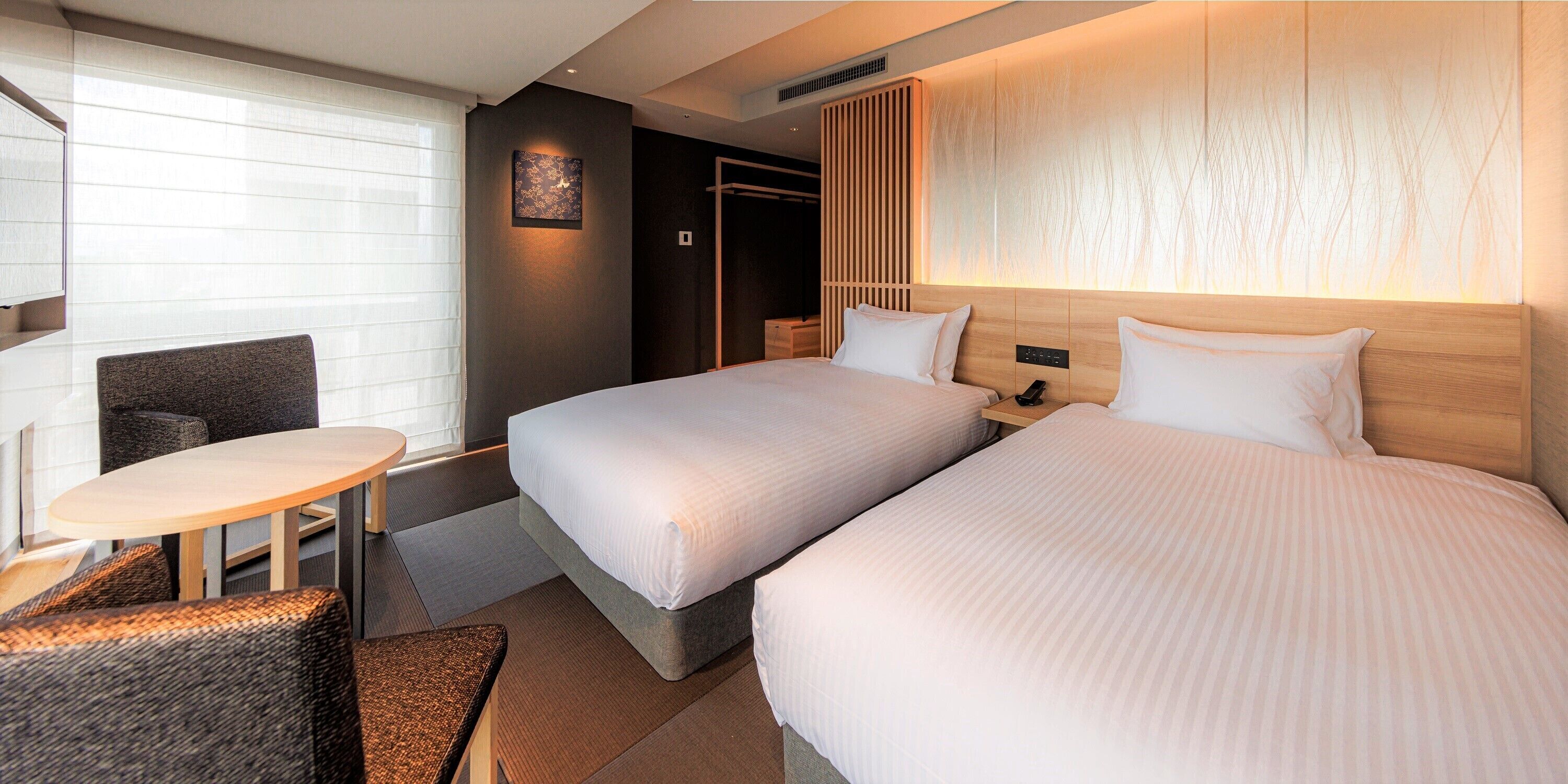 A hotel room with two beds, a small table, and a chair.