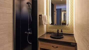 A modern bathroom with a dark shower, a sink with a round basin, and a mirror above it.