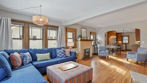 Ein großzügiges Wohnzimmer mit einem blauen Sofa, einem gestreiften Hocker und einem Essbereich mit Tisch und Stühlen.