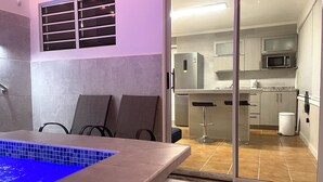 Une salle de bain moderne avec une piscine illuminée de lumière bleue, un espace douche et une porte coulissante en verre donnant sur une cuisine équipée d’un four à micro-ondes et d’une machine à café.