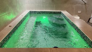 Une piscine rectangulaire dotée d’un éclairage vert, de murs carrelés et d’une rambarde métallique.