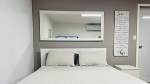 Un lit bien fait, recouvert d’une couette blanche, un grand miroir au-dessus et une citation inspirante sur le mur.