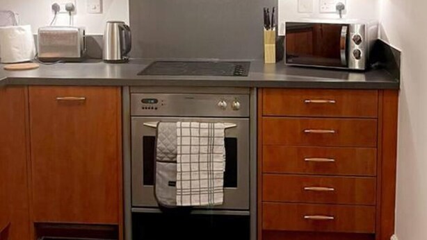 Una cocina con armarios de madera, una campana extractora de acero inoxidable, un microondas, un tostador y una tetera.