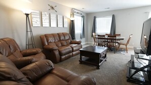 Un salon avec un canapé en cuir marron, une table basse, une table à manger avec des chaises et un téléviseur.