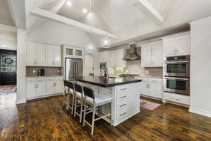 A modern kitchen with white cabinetry, a central island with bar stools, stainless steel appliances, and a wooden floor.