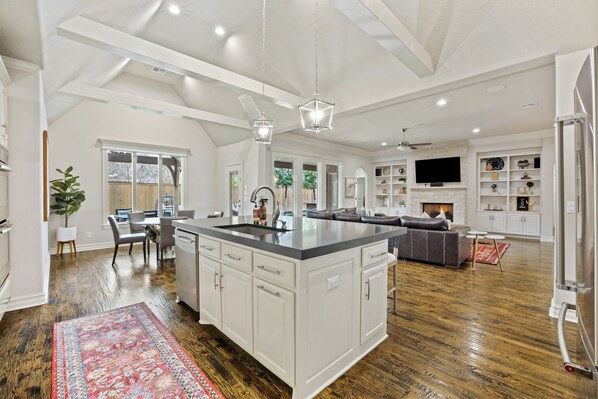 A spacious kitchen with a large island, white cabinetry, and a modern chandelier.