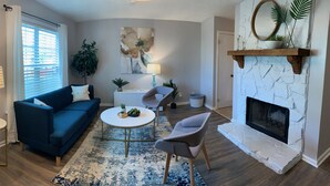 Un salon avec un canapé bleu, une table basse ronde, une cheminée et un grand tableau abstrait accroché au mur.