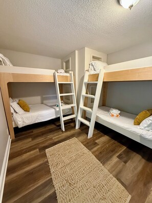 A room with two bunk beds, a white ladder, a patterned rug, and wooden flooring.