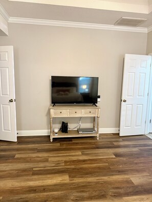 Ein Zimmer mit einem Fernseher auf einem Holzboden, einer weißen Tür links und einer weißen Tür rechts.