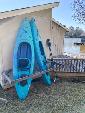 Deux kayaks appuyés contre un bâtiment, avec une jetée qui s’avance dans une étendue d’eau.