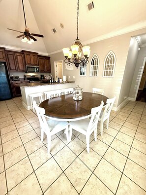 A kitchen with a central island, white chairs, a chandelier, and a ceiling fan.