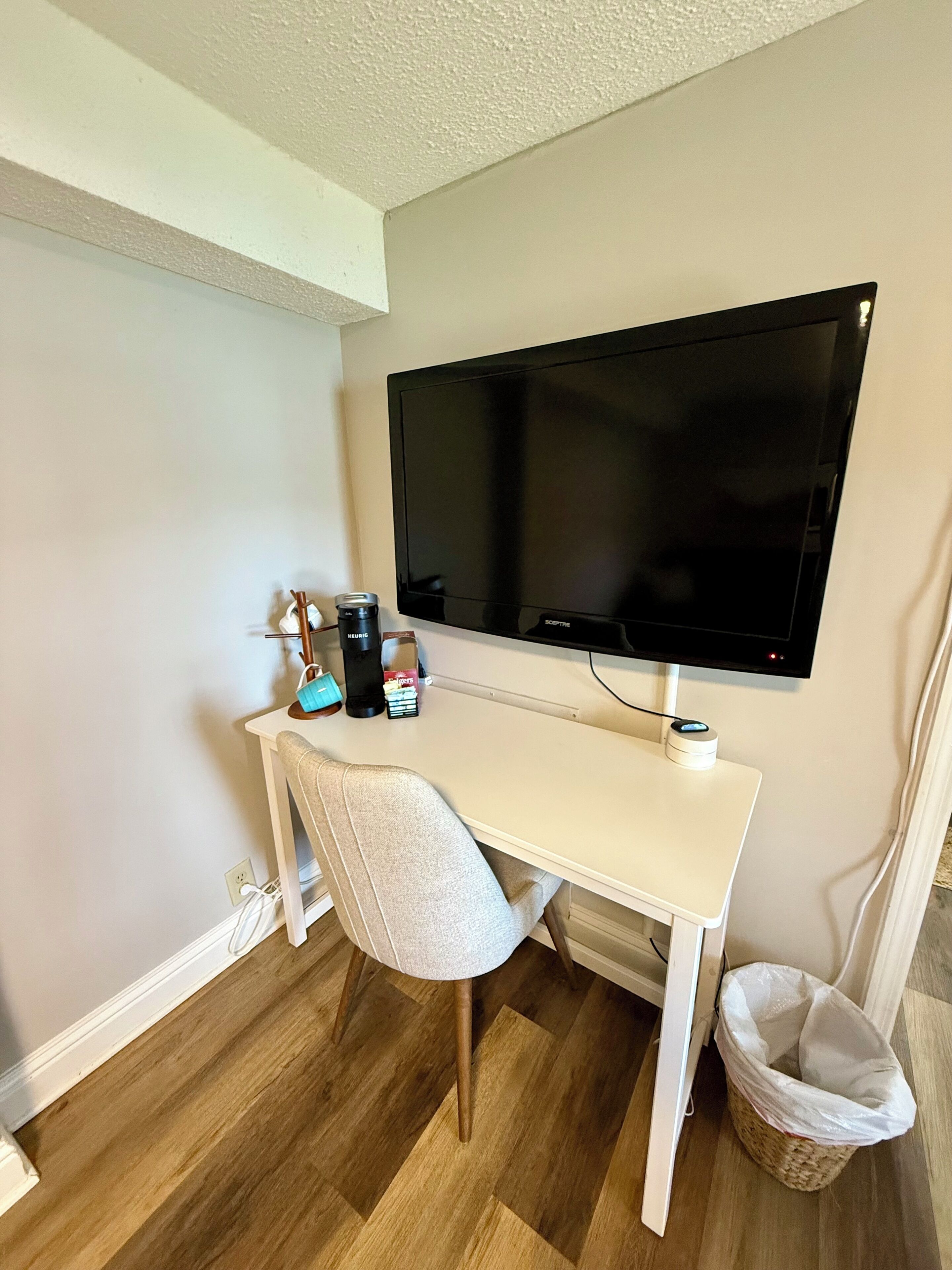 A small, white desk with a computer monitor, a chair, and a waste basket.
