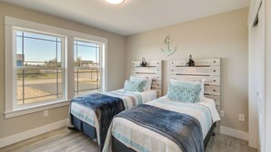 Une chambre avec deux lits, de grandes fenêtres, une vue sur l’extérieur et un luminaire au plafond.