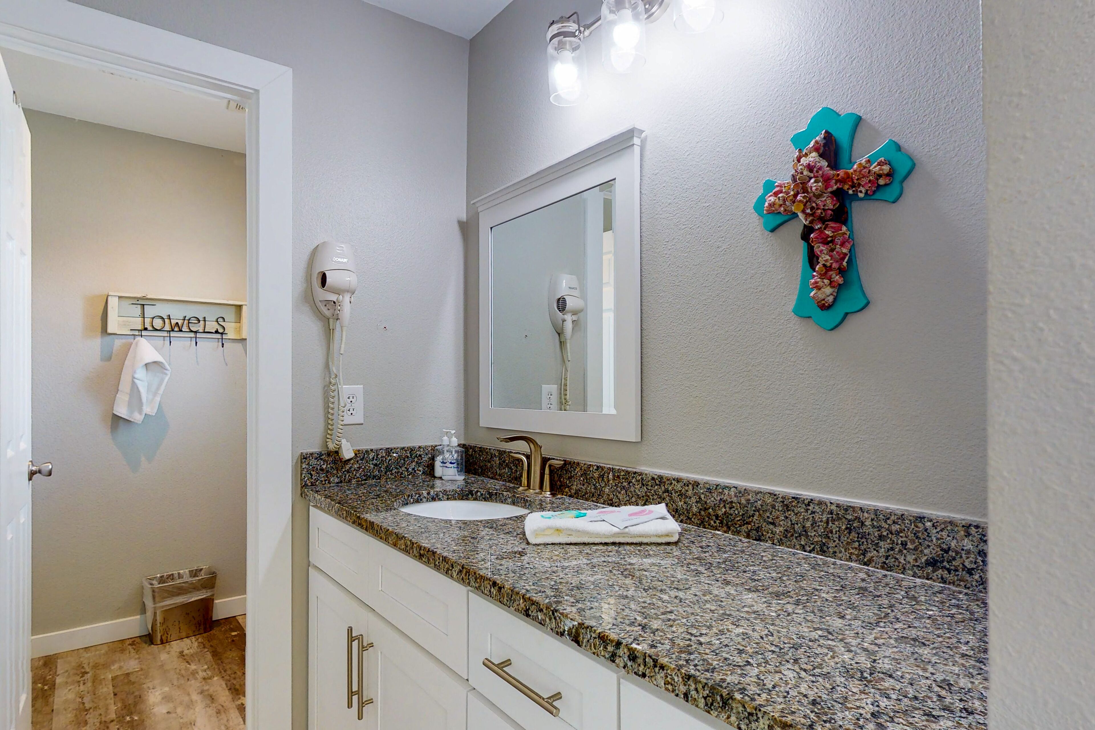 A bathroom with a granite countertop, a white sink, a mirror, a hairdryer, and a towel rack.