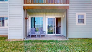 A two-story house with a balcony, sliding glass doors, and a small patio with two chairs. - 1st Floor, Pets Friendly, Shared Pool Hot Tub, Near Marina (Port Aransas)