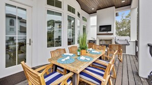An outdoor patio with a wooden table, chairs, and a television mounted on the wall.