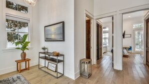 A hallway with a wooden floor, a framed picture on the wall, a potted plant, a metal console table, and a welcome sign.