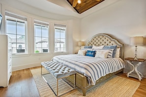 Quarto com cama, um banco, mesa de cabeceira, luminária e janela com vista.