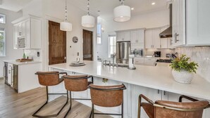 A modern kitchen with white cabinetry, stainless steel appliances, and a central island with bar stools.