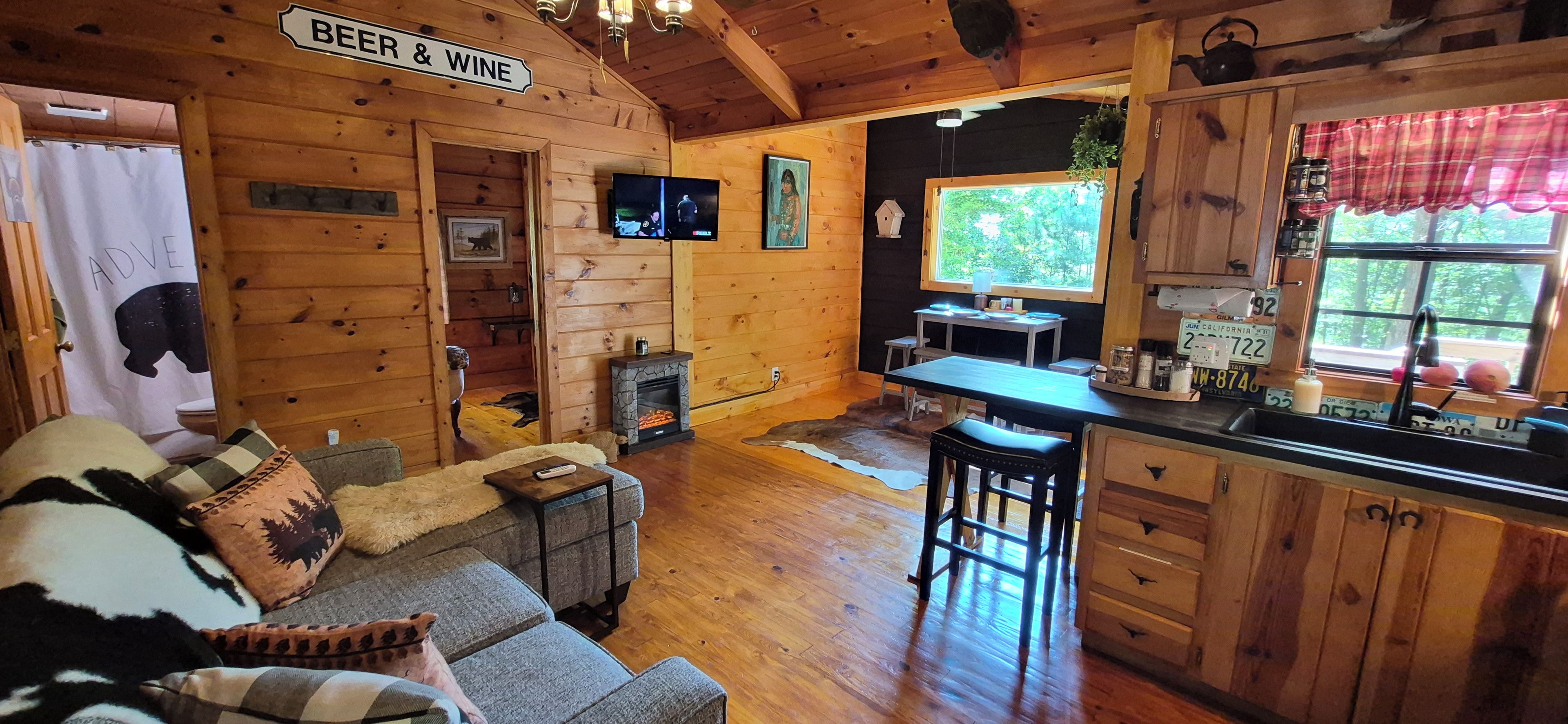 L’intérieur d’un chalet accueillant comprend un espace de vie, une cheminée, une cuisine et un panneau indiquant que de la bière et du vin sont en vente.