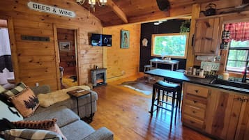 L’intérieur d’un chalet accueillant comprend un espace de vie, une cheminée, une cuisine et un panneau indiquant que de la bière et du vin sont en vente.