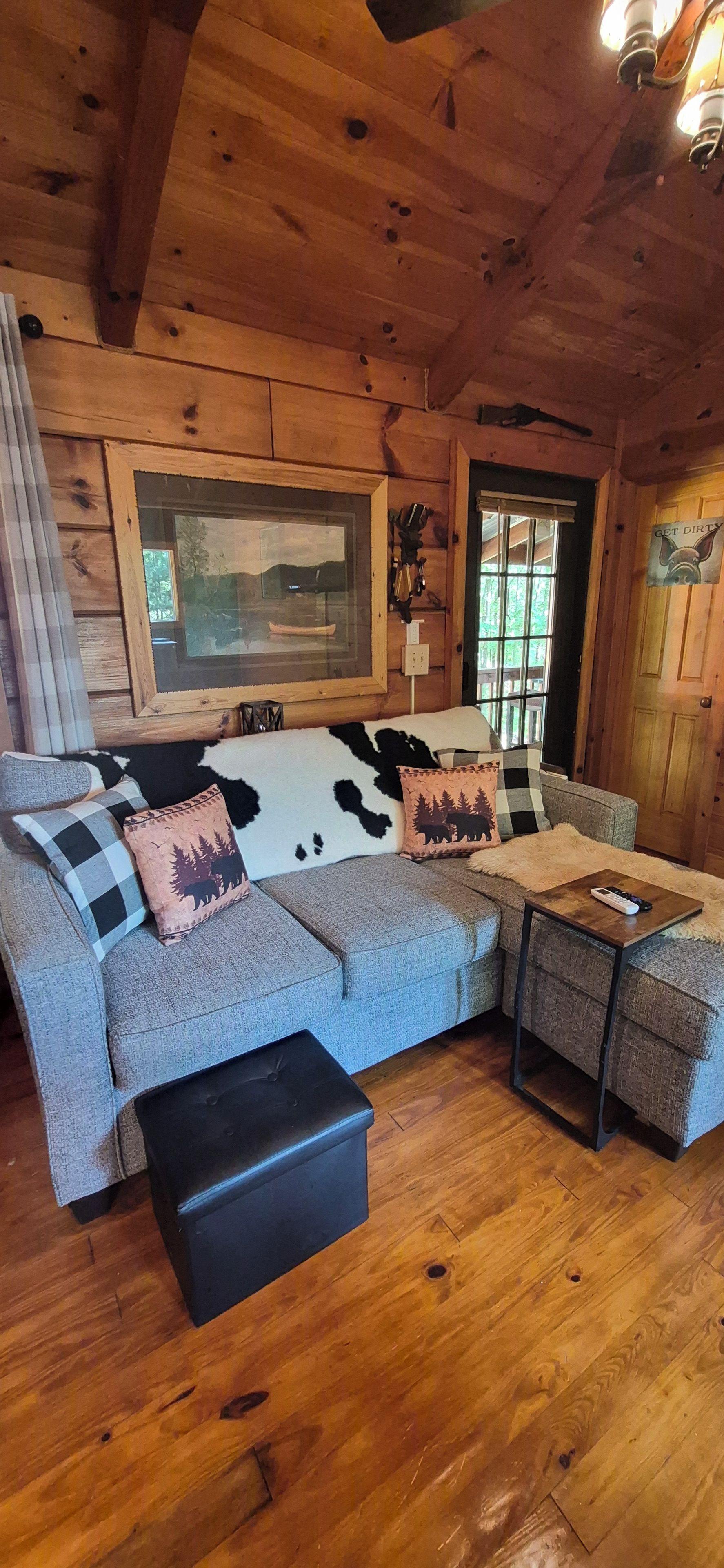 L’intérieur d’un chalet accueillant, avec un canapé d’angle, une petite table et une fenêtre donnant sur un lac.