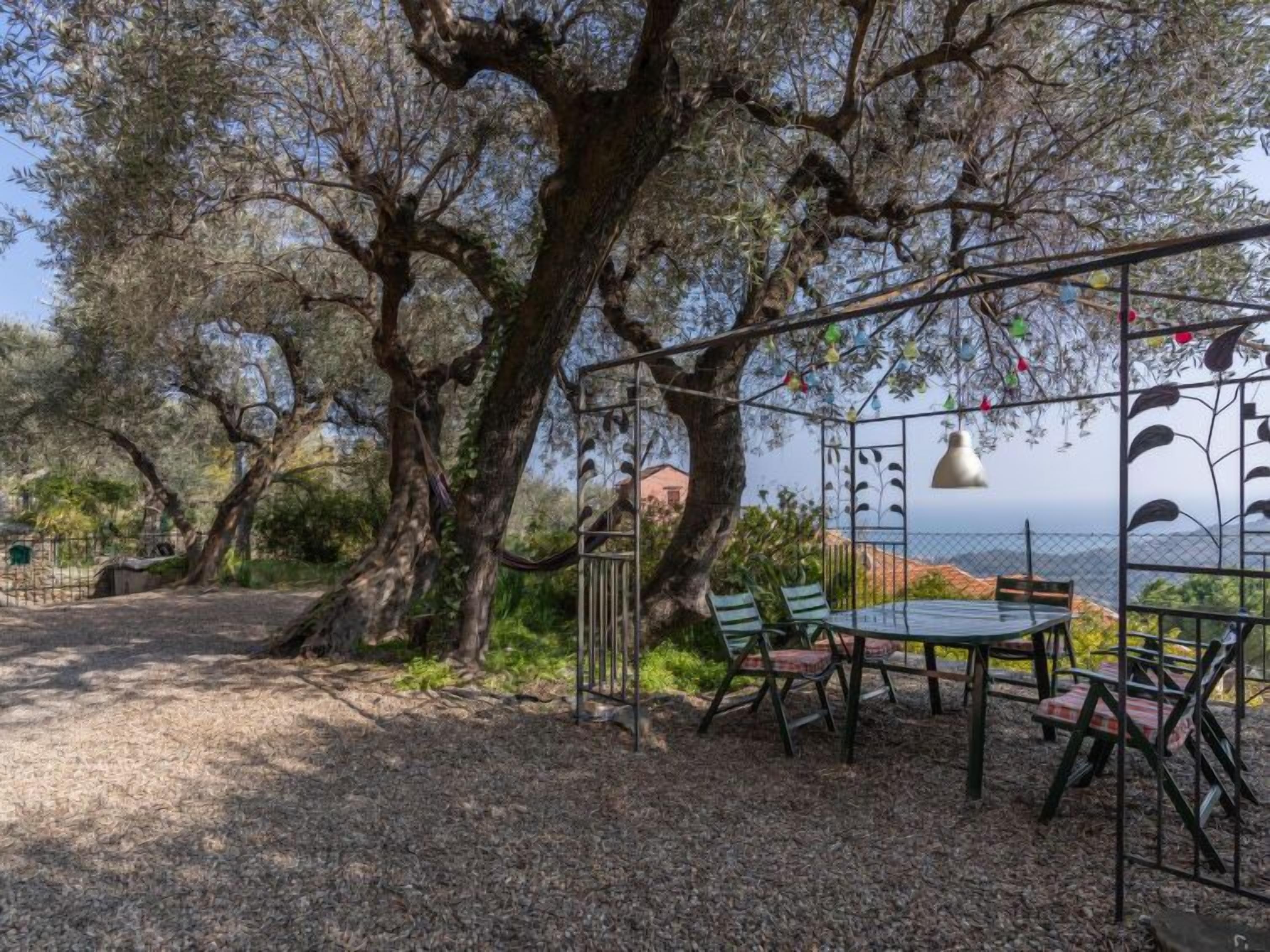 An outdoor seating area with a table and chairs, surrounded by trees and overlooking a body of water.