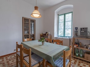 Un coin repas avec une table dressée pour quatre personnes, des chaises, un luminaire suspendu, une fenêtre avec vue et une machine à café.