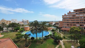 A resort with a swimming pool surrounded by palm trees, a playground, and a view of the sea. - Charming studio for rent in Roses, Costa Brava! Sleeps 3, modern amenities, pool, free Wi-Fi, close to beach. (Roses)