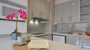 A modern kitchen with white cabinets, a built-in oven, and a sink. There is a plant with pink flowers on the counter, and two cups and a book. - Charming studio for rent in Roses, Costa Brava! Sleeps 3, modern amenities, pool, free Wi-Fi, close to beach. (Roses)