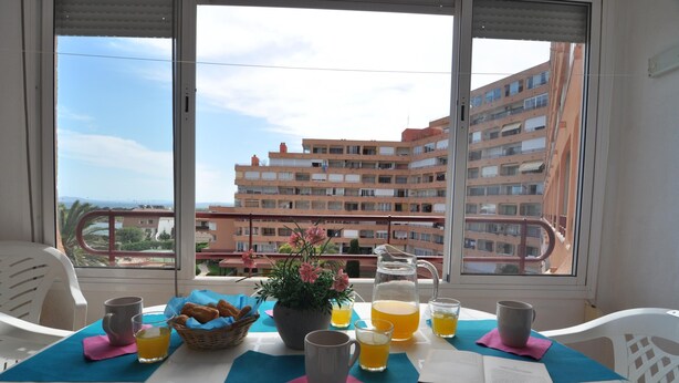 A balcony with a table set for breakfast, including a pitcher of orange juice, a mug, and a book. - Charming studio for rent in Roses, Costa Brava! Sleeps 3, modern amenities, pool, free Wi-Fi, close to beach. (Roses)