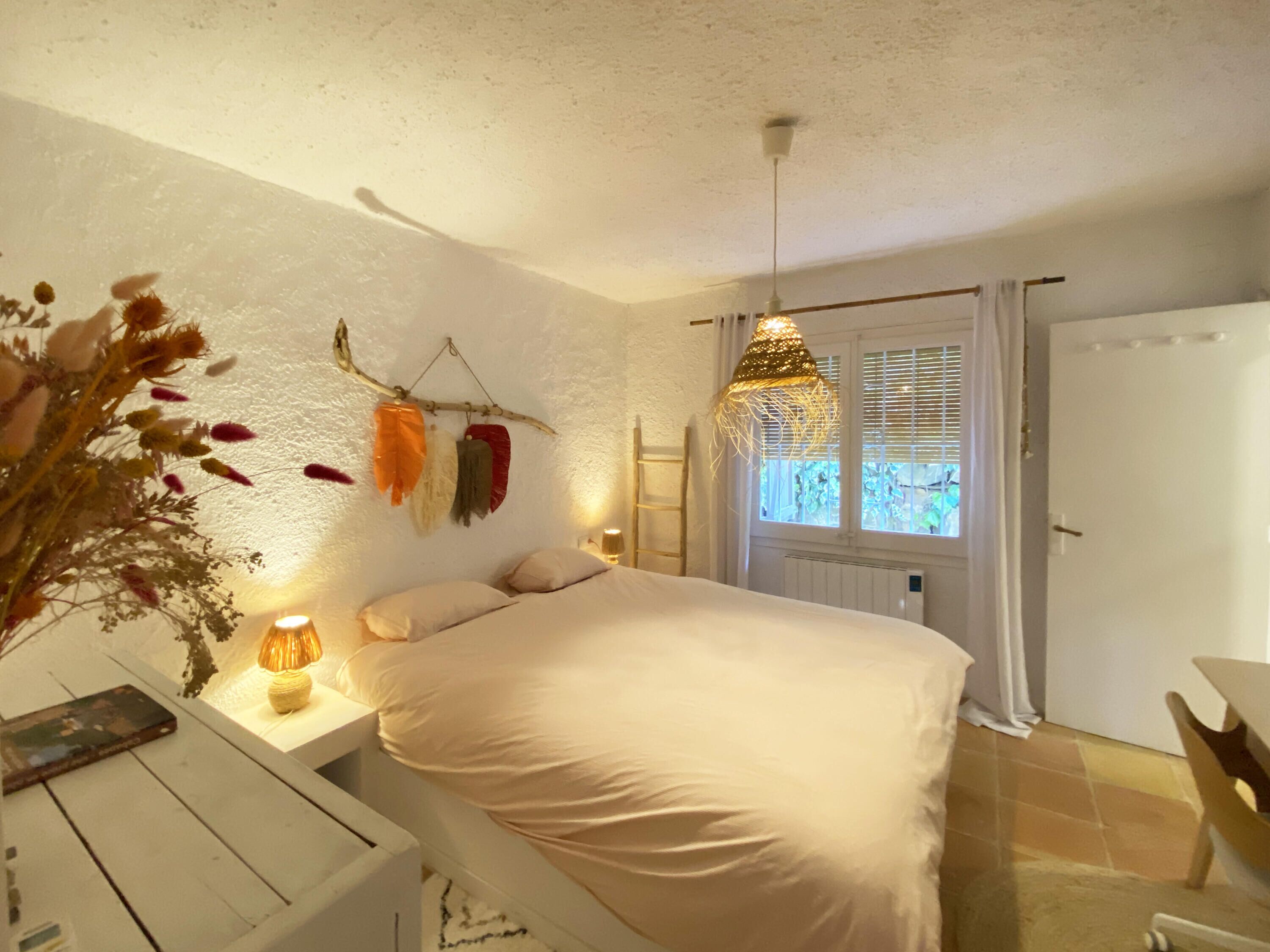 A bedroom with a bed, bedside table, lamp, and a window with curtains.