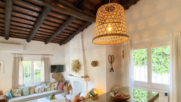 Una sala de estar acogedora con techo de madera, una mesa de vidrio y un ventanal con follaje exterior.