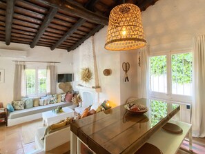 Una sala de estar acogedora con techo de madera, una mesa de vidrio y un ventanal con follaje exterior.