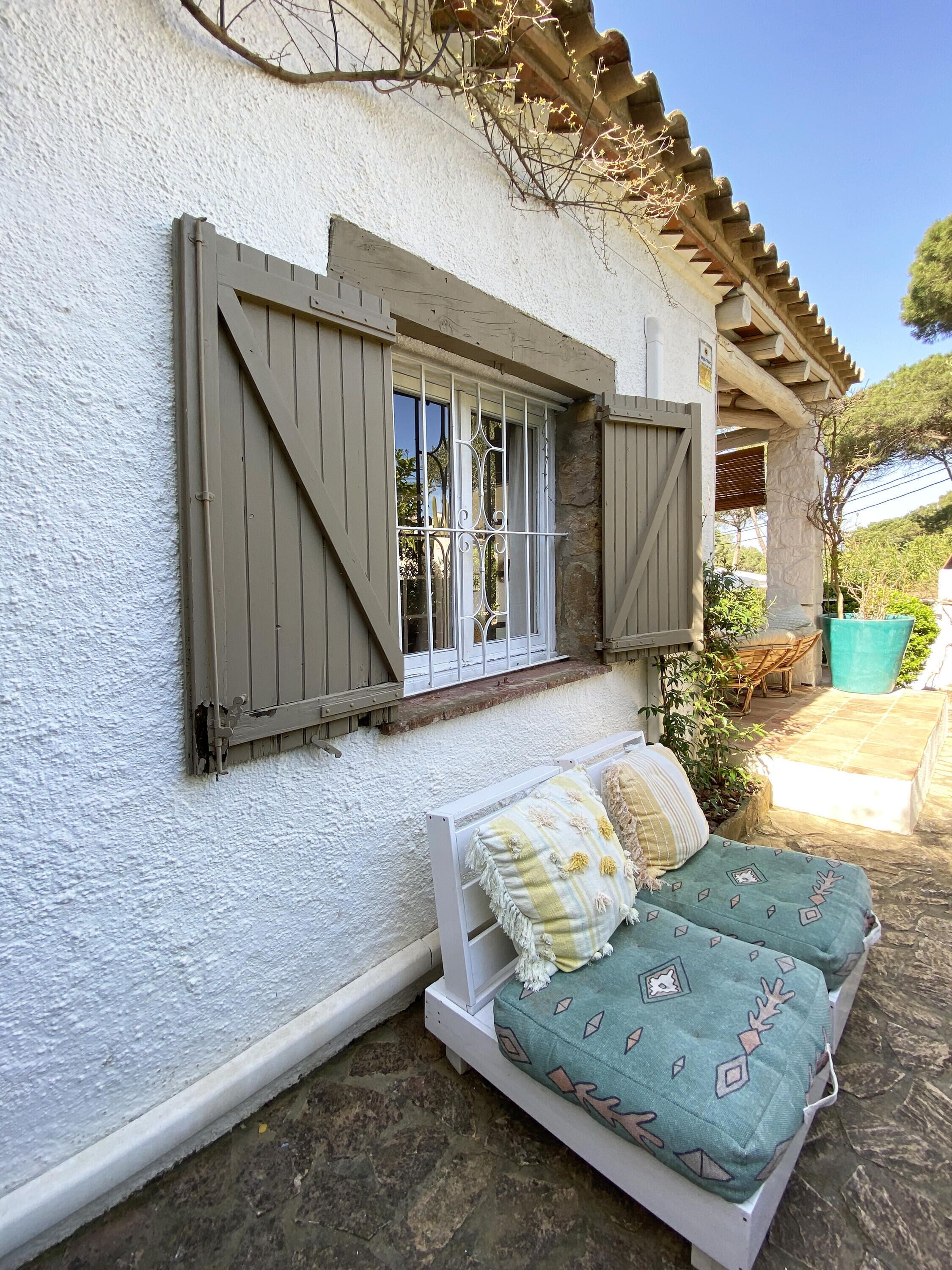 A white building with a window and shutters, a stone floor, and a bed with patterned bedding.