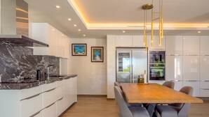 Uma cozinha moderna com armários brancos, bancada de mármore e uma mesa de jantar de madeira com cadeiras.