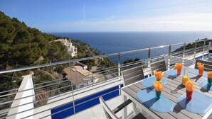 Um terraço com piscina, área de estar ao ar livre e vista para o mar e colinas.