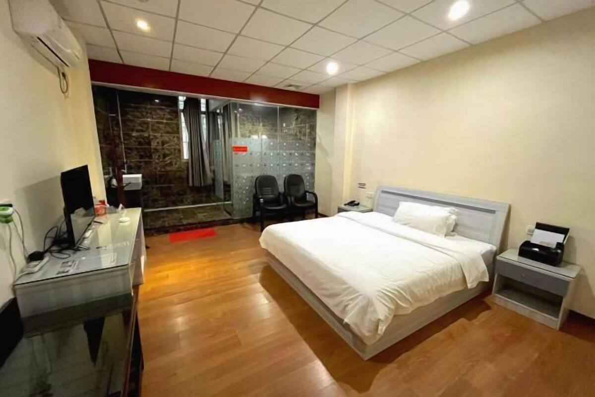 A hotel room with a bed, a desk, a chair, a TV, and a bathroom with a glass door.