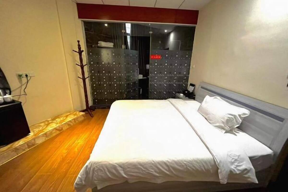 A hotel room with a bed, a wooden floor, a coat rack, and a wall-mounted TV.