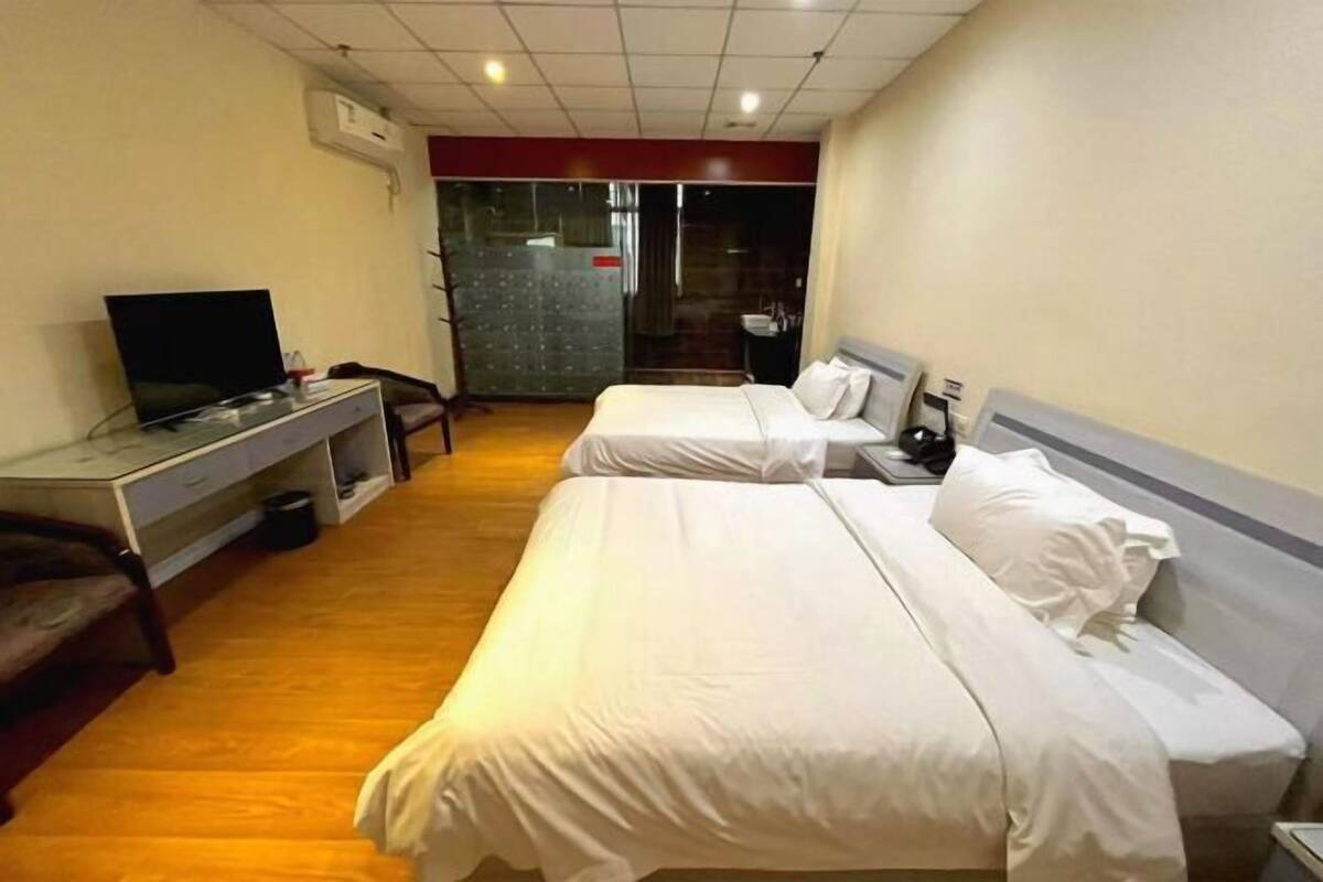 A hotel room with two beds, a desk with a TV, a chair, and a small table.