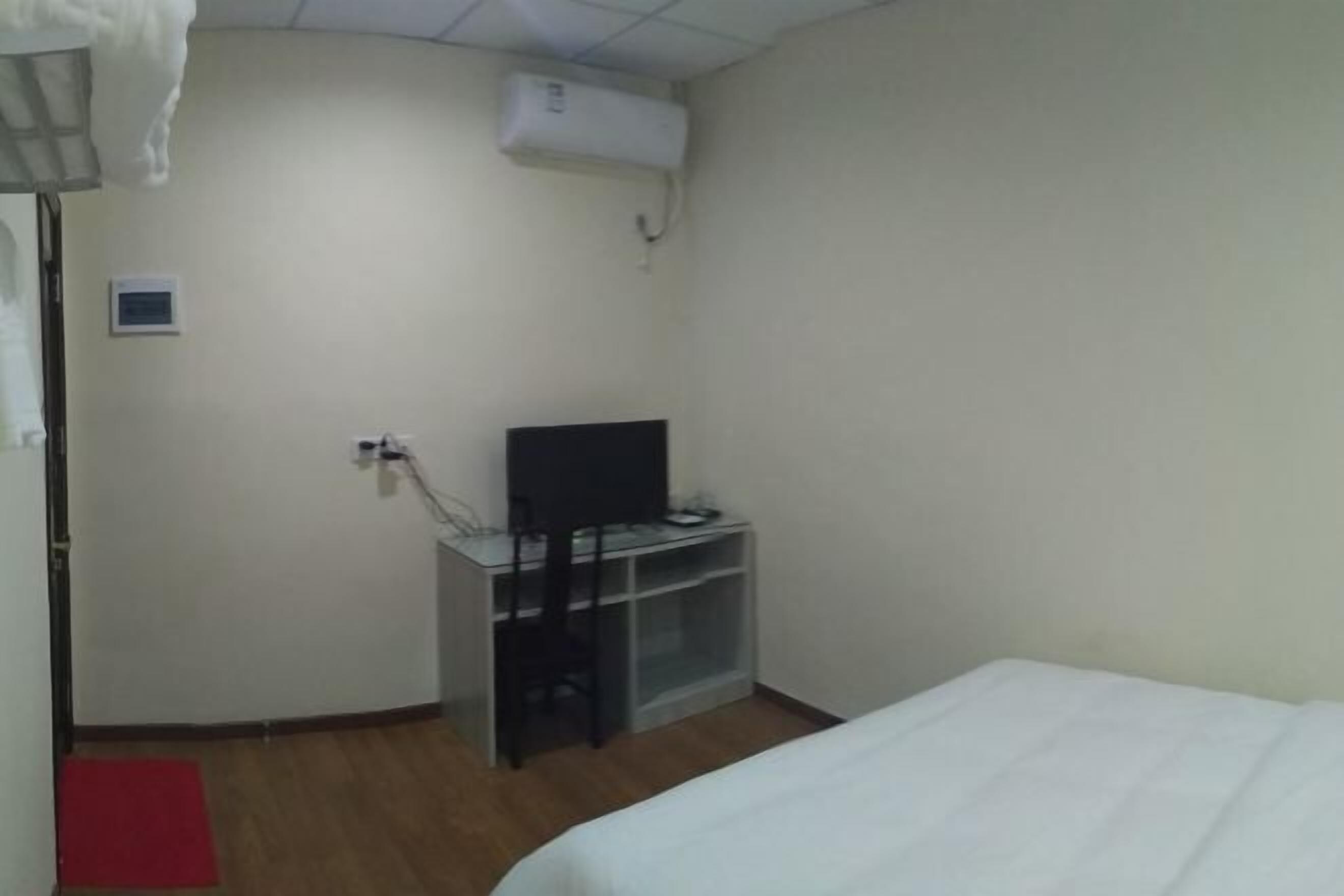 Een kamer met een bed, een bureau met een stoel, een televisie en een airconditioner.