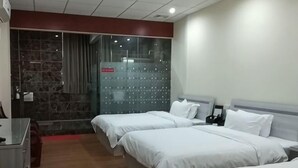 Ein Hotelzimmer mit drei Betten, einem Schreibtisch, einem Stuhl und einer Duschkabine.
