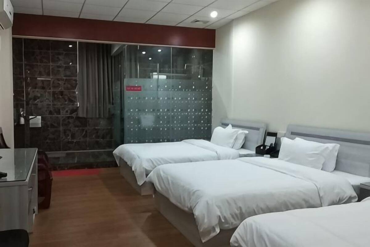 A hotel room with three beds, a desk, a chair, and a shower area.