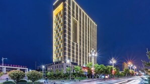 Un edificio hotelero alto e iluminado, de diseño moderno, rodeado de árboles y farolas.