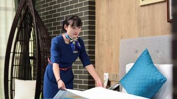 A person in a blue uniform cleaning a bed with a blue bedspread and a white pillow.