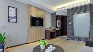 Une chambre d’hôtel moderne dotée d’un téléviseur à écran plat fixé au mur, d’un mur d’accent en bois, d’une table basse ronde sur laquelle se trouve un plateau avec des tasses à thé, et d’une plante en pot.