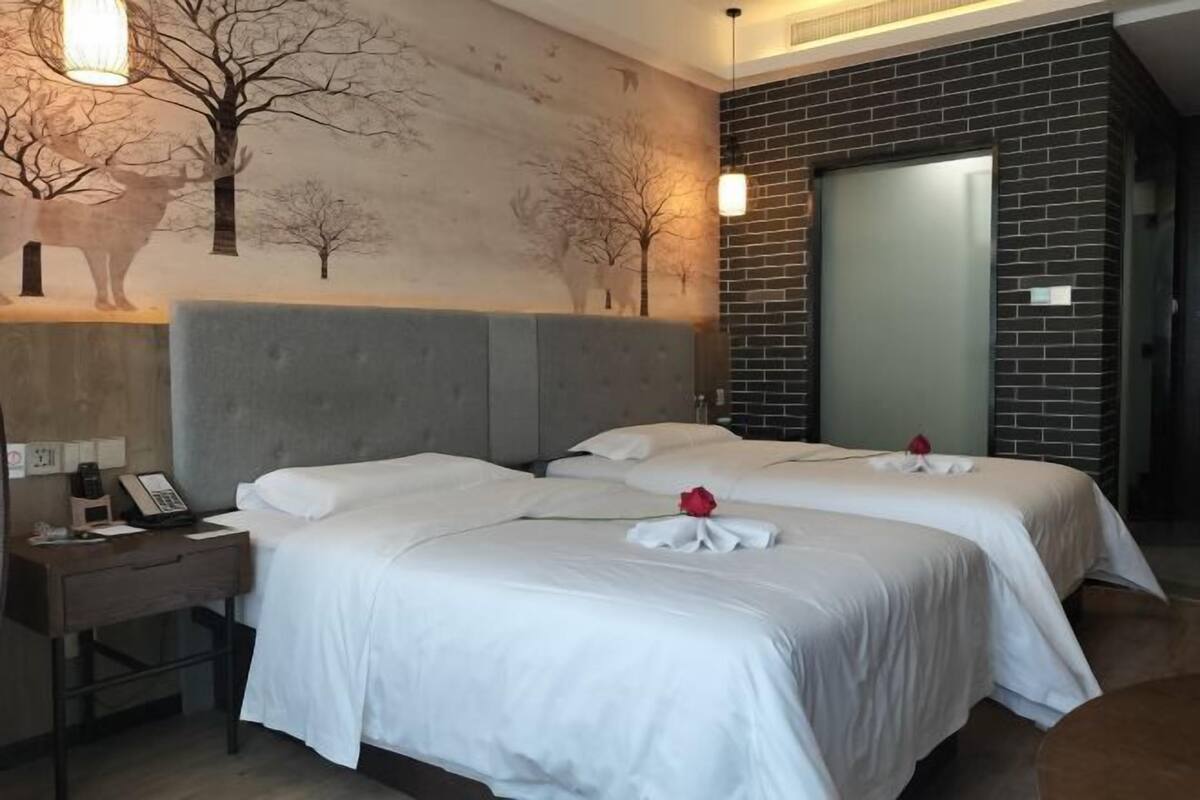 A hotel room with two beds, a nightstand, a telephone, and a wall with a tree mural.