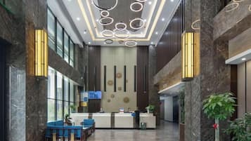 A hotel lobby with a reception desk, seating area, and a large plant.